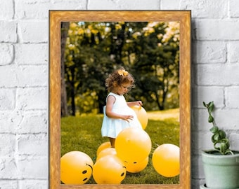 Può includere: Una bambina con un vestito bianco gioca con palloncini gialli in un'area erbosa. I palloncini hanno facce sorridenti.