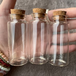 May include: Three clear glass bottles with cork stoppers. The bottles are empty and have a round shape.