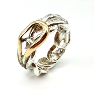 May include: A silver-toned ring with a gold-colored accent. The ring features a chain-link design with a gold-colored oval shape in the center. The ring is set against a white background.