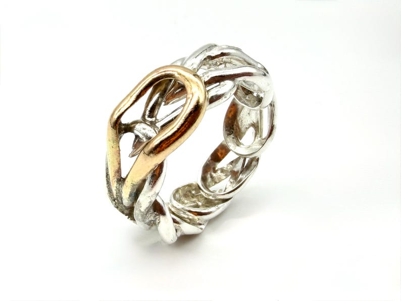 May include: A silver-toned ring with a gold-colored accent. The ring features a chain-link design with a gold-colored oval shape in the center. The ring is set against a white background.
