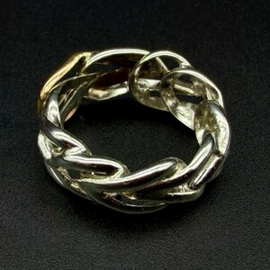 May include: A silver-toned chain link ring. The ring features a continuous loop of interlocking chain links, with a gold-colored section visible. The ring is set against a dark background.