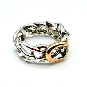 May include: A silver-toned chain link ring with a gold-colored accent. The ring features a chunky, interlocking design, with a polished finish. The gold accent is a rectangular shape, adding a contrasting element to the overall design.