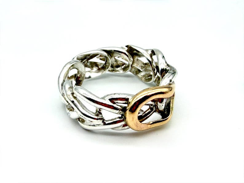 May include: A silver-toned chain link ring with a gold-colored accent. The ring features a chunky, interlocking design, with a polished finish. The gold accent is a rectangular shape, adding a contrasting element to the overall design.