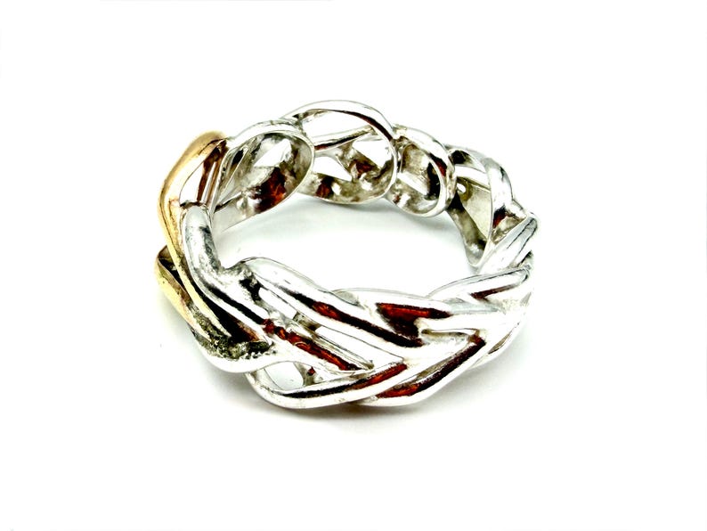 May include: A silver ring with a woven chain design. The ring has a gold-colored section on one side. The ring is set against a white background.