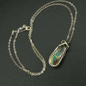 May include: Silver necklace with a pendant featuring a colorful opal stone. The opal displays shades of green, blue, and brown. The pendant is encased in a silver setting, and the chain is a delicate link style.
