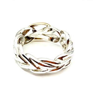 May include: A silver-colored ring with a braided design. The ring has a gold-colored section in the center. The ring is set against a white background.