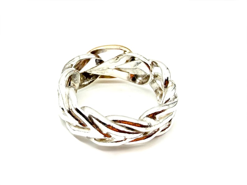May include: A silver-colored ring with a braided design. The ring has a gold-colored section in the center. The ring is set against a white background.