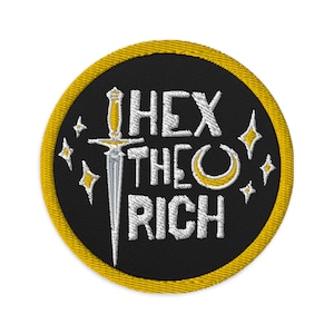 May include: A black and gold round embroidered patch with the text "Hex the Rich" in white lettering. A silver dagger and a crescent moon are also embroidered on the patch.