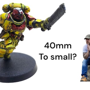 May include: A yellow and red miniature figurine of a space marine with a bolter and chainsword, mounted on a black base. The text "40mm To small?" is visible. A man is sitting on a rock.