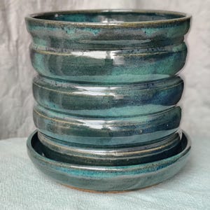 May include: A stack of handmade ceramic bowls and a matching saucer. The bowls are glazed in shades of teal and dark blue, with a glossy finish. The stacked design adds a unique, artistic touch to the kitchenware.