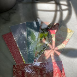 Könnte beinhalten: Ein Set mit sechs bunten Lesezeichen mit verschiedenen Mustern. Die Lesezeichen sind aus klarem Kunststoff mit einer strukturierten Oberfläche. Die Muster umfassen ein Blumenmuster, eine Karte und ein geometrisches Muster.