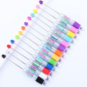 May include: A set of 12 multi-colored retractable ballpoint pens with clear barrels and colorful ink refills. The pens have a variety of colors including red, orange, yellow, green, blue, purple, pink, and black.