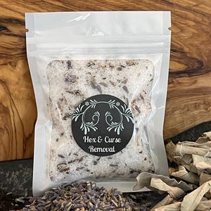 Peut inclure: Un sachet refermable blanc rempli de sel de bain blanc et de fleurs de lavande séchées. Un autocollant rond noir avec le texte "Hex & Curse Removal" est sur le devant du sachet.