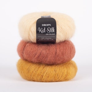 May include: Three skeins of yarn in different colors: beige, brown, and yellow. The yarn is soft and fluffy, and the label reads "DROPS Kid-Silk UNI COLOUR Soft & luxurious in Super Kid Mohair & Silk."