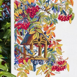 May include: Cross-stitch pattern of a birdhouse with two bluebirds, surrounded by red berries and yellow leaves. The pattern is on white Aida cloth and signed "MEREJKA".