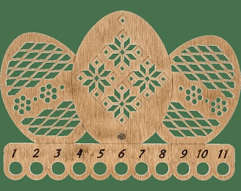 May include: Wooden egg-shaped needle minder with 11 numbered holes for storing needles. The minder features a geometric design with a snowflake pattern in the center.