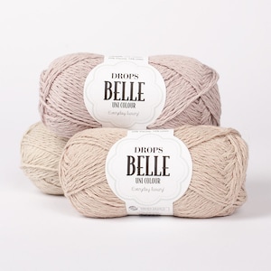 May include: Three skeins of Drops Belle yarn in beige and light pink. The yarn is made of 53% viscose and 47% linen. The label reads "Drops Belle Uni Colour Everyday luxury!"