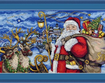 May include: Santa Claus in a red suit and white beard carries a large sack of gifts on his back. He is walking with a lantern in one hand and a reindeer-drawn sleigh in the other. The scene is set against a snowy town with a starry night sky.