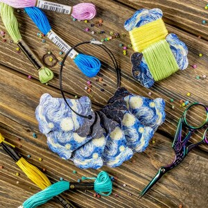 Op de afbeelding: Een set borduurgaren-spoelen met een Sterrennacht-ontwerp. De spoelen zijn in een cirkel gerangschikt en worden bij elkaar gehouden door een zwart koord. De spoelen zijn omringd door kleurrijke kralen en borduurgaren.