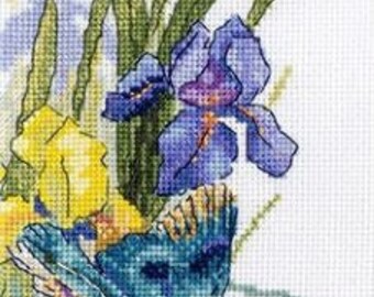 May include: A cross-stitch pattern featuring a blue bird perched on a stem of yellow and purple irises. The bird is facing the left side of the image and has a long, pointed beak. The irises are in full bloom and have delicate petals.