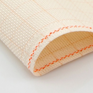 May include: Close-up of a beige fabric with a fine weave and orange stitching along the edges.