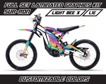 May include: A Sur-Ron Light Bee X electric dirt bike with a custom tie-dye graphic kit. The bike is white with a rainbow tie-dye pattern. The graphics kit is customizable with different colors.  FULL SET LAMINATED GRAPHICS KIT SUR-RON LIGHT BEE X LIE CUSTOMIZABLE COLORS