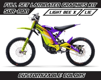 May include: A yellow, purple, and orange graphic kit for a Sur-Ron Light Bee X electric motorcycle. The kit includes a full set of laminated graphics with the Sur-Ron logo and the words "Light Bee X" and "Lie". The graphics are customizable in color.