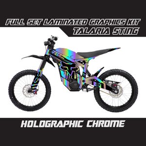 Op de afbeelding: Een zwart-witte elektrische dirt bike met een holografische chromen afwerking. De fiets heeft een Fox Racing logo en de woorden "Talaria Sting" aan de zijkant. De fiets staat op een witte achtergrond.