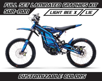 May include: A blue and black Sur-Ron Light Bee X electric dirt bike with custom graphics. The bike has a black seat, black handlebars, and black wheels. The graphics are blue, white, and black. The bike is on a white background.  The text "SUR-RON" and "LIGHT BEE X" is visible on the bike.