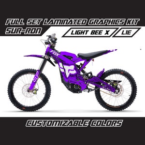 May include: Purple Sur-Ron Light Bee X electric dirt bike with a Fox Racing graphic kit. The bike has a leopard print design and the words "FULL SET LAMINATED GRAPHICS KIT" and "CUSTOMIZABLE COLORS" are printed on the image.