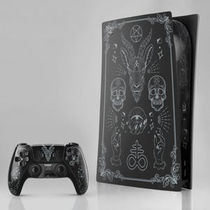 May include: Black gaming console and controller set with intricate white illustrations of skulls, a goat head, and other occult symbols. The console has a vertical design, and the controller is positioned in front.