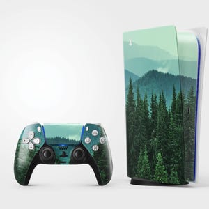 May include: A gaming console and controller set featuring a nature-themed design. The console and controller are adorned with a landscape of green trees and mountains. The controller has white buttons and black accents.