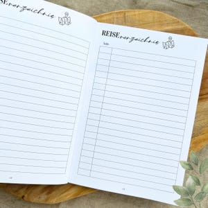 May include: A white notebook with a black and white map icon and the text "REISE verzeichnis" on the cover. The notebook is open to a blank page with lines for writing.
