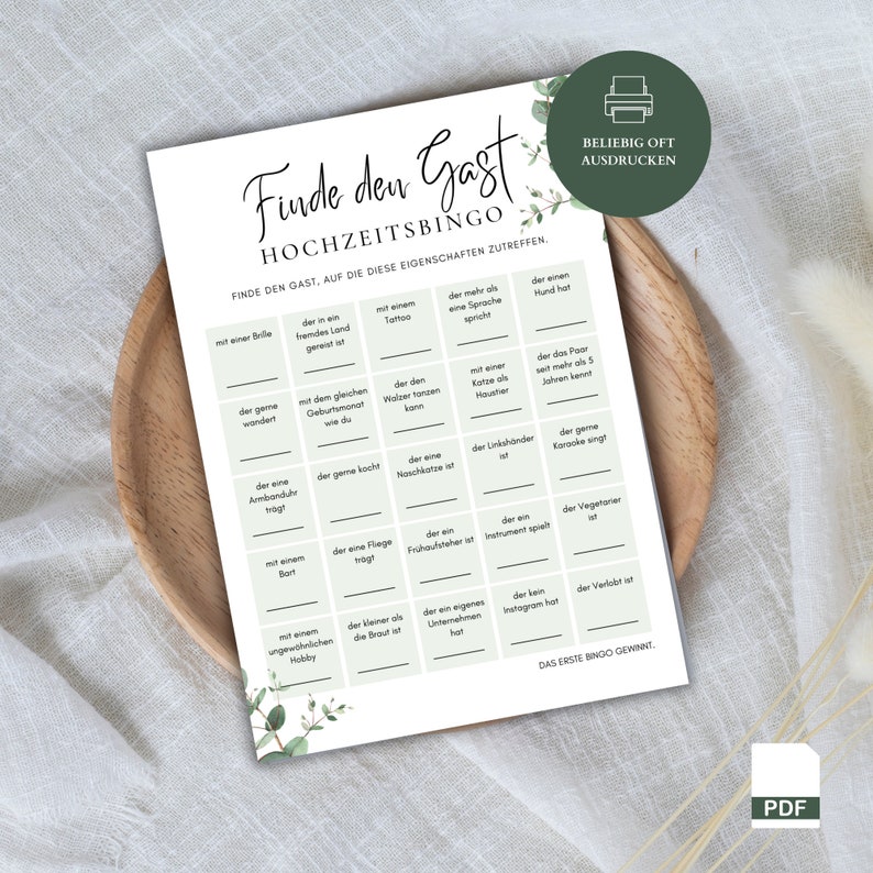 May include: A printable wedding game bingo card with the title "Finde den Gast" (Find the Guest) and the instructions "Find the guest who matches these characteristics". The card has a green and white colour scheme with a floral design.
