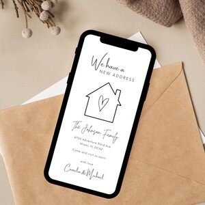 May include: A white smartphone with a black frame displays a new address announcement for the Johnson family. The announcement features a simple house illustration with a heart inside and includes their new address: 4700 Adventure 32nd Ave, Miami, FL 33142. The message encourages visitors to come and visit soon, signed with love by Camelia & Michael.