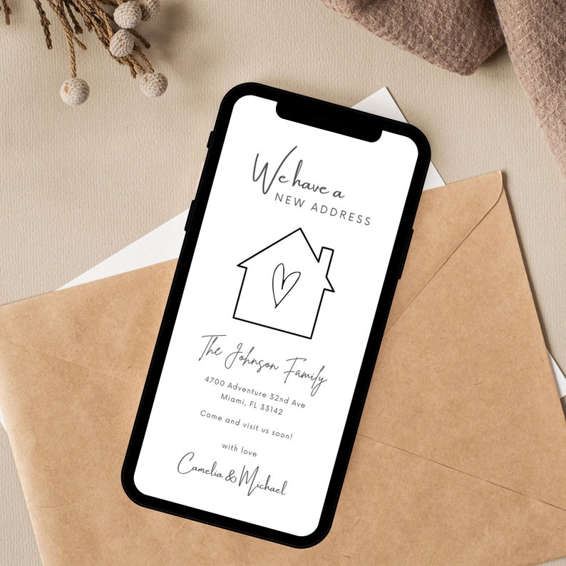 May include: A white smartphone with a black frame displays a new address announcement for the Johnson family. The announcement features a simple house illustration with a heart inside and includes their new address: 4700 Adventure 32nd Ave, Miami, FL 33142. The message encourages visitors to come and visit soon, signed with love by Camelia & Michael.
