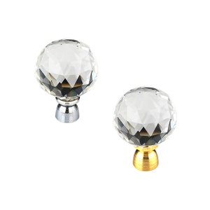 May include: Two crystal cabinet knobs with faceted surfaces. One knob has a silver base and the other has a gold base.