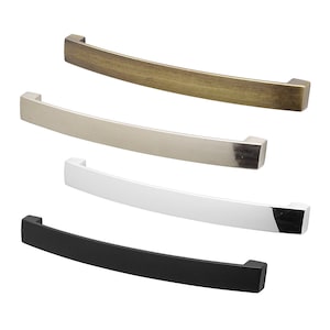 May include: Four cabinet pulls in different finishes: antique brass, nickel, white and black. Each pull is curved and has a rectangular shape.