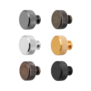 May include: Six round cabinet knobs in different finishes: black, brass, nickel, antique brass, and two shades of bronze. Each knob has a textured, knurled surface.