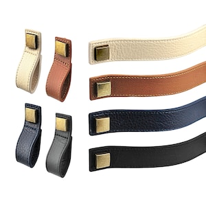 May include: Four leather handles with brass fittings in various colours: beige, brown, dark blue, and grey. The handles are designed for furniture or bags.