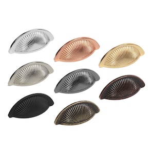 May include: A set of eight cabinet pulls in various finishes, including polished nickel, copper, brass, black, and antique brass. Each pull features a fan-shaped design with a curved shape.