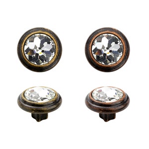 May include: Four crystal cabinet knobs with a round, faceted crystal set in a metal frame. Two knobs have a dark bronze finish and two knobs have a copper finish.