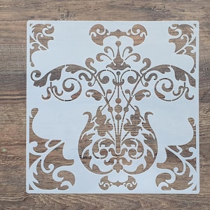 Könnte beinhalten: Weiße Kunststoffschablone mit einem dekorativen floralen Design. Das Design verfügt über komplizierte Wirbel und Kurven, die ein Damastmuster erzeugen.
