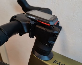 May include: A black bicycle handlebar with a black and red Sigma bike computer mounted on top. The handlebar is attached to a green and black bicycle frame with the words "BACK ROAD" printed on the frame.