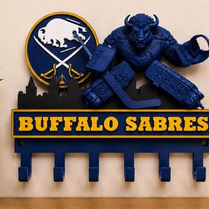 May include: A blue and yellow Buffalo Sabres key holder featuring the team logo, a hockey player figure, and the words "Buffalo Sabres." The key holder has six hooks for hanging keys.