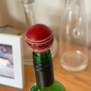 May include: A red leather cricket ball bottle stopper on a green wine bottle.