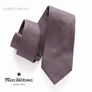 Può includere: Una cravatta di seta grigia scura con il testo "Giorgio Armani" e "Max Stötzner GEGR. 1910" stampato sull'etichetta.