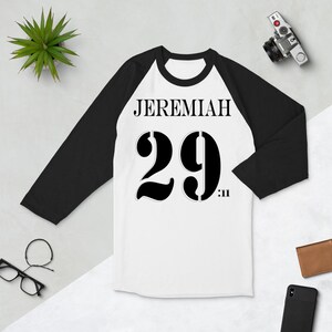 May include: White and black baseball style t-shirt with the text "JEREMIAH 29:11" printed on the front.