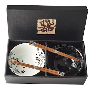 Può includere: Una confezione regalo nera contenente due ciotole in ceramica e due paia di bacchette in legno. Una ciotola è bianca con disegni floreali neri, l'altra è nera con disegni floreali bianchi. Le bacchette sono marroni.
