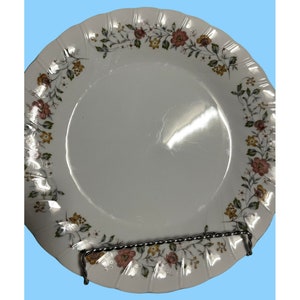 May include: White ceramic dinner plate with a floral pattern in shades of pink, yellow, and green. The plate has a scalloped edge.